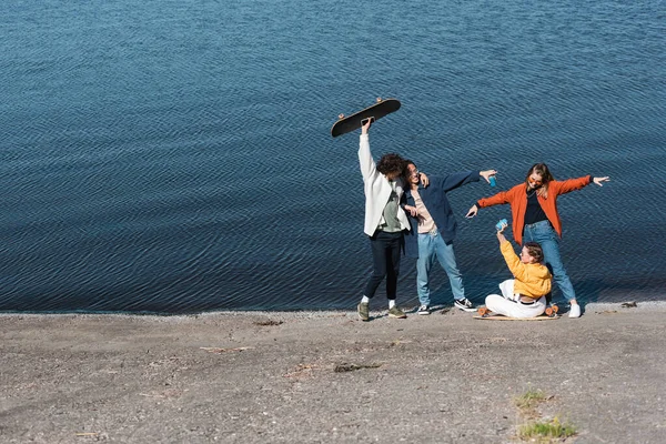 Cheerful multiethnic skaters having fun on embankment near river — Stock Photo