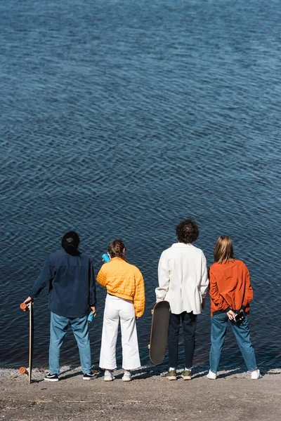 Back view of friends in stylish clothes standing on river bank — Stock Photo