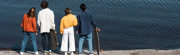 Vue arrière des patineurs jeunes et branchés debout sur le bord de la rivière, bannière — Photo de stock