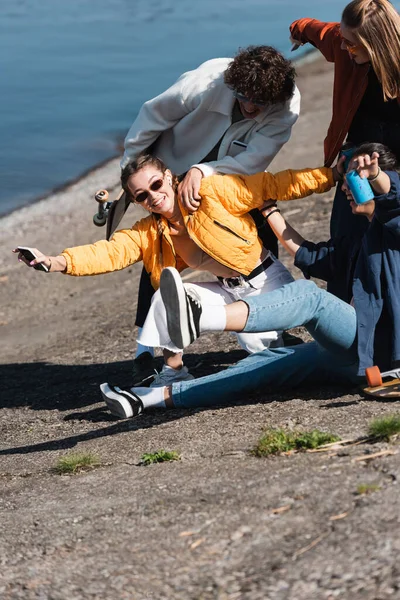 Cheerful woman with mobile phone having fun with friends on embankment — Stock Photo