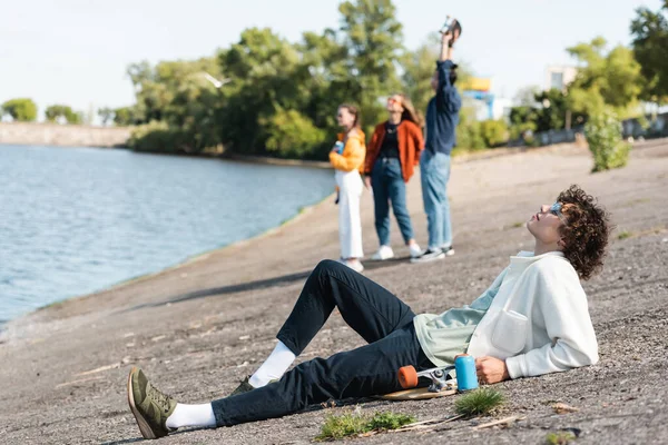 Toute la longueur du jeune patineur relaxant sur le remblai près des amis flous — Photo de stock