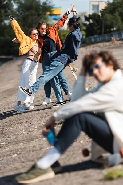 Amis multiethniques joyeux s'amuser en plein air près de l'homme assis sur le premier plan flou — Photo de stock