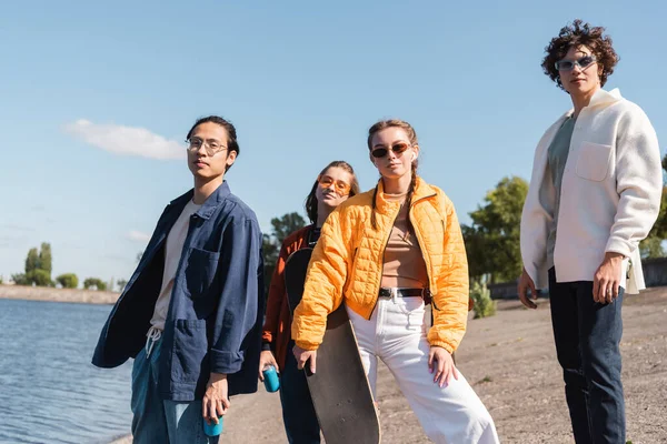 Amigos multiétnicos con estilo en gafas de sol mirando a la cámara al aire libre - foto de stock