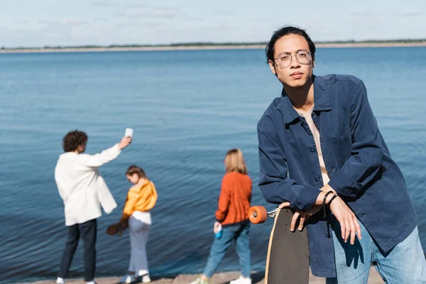 Азіатський чоловік з довгим бортом дивиться на камеру біля розмитих друзів і річки — стокове фото