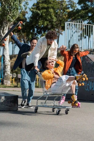 Eccitati amici multietnici si divertono con il carrello della spesa nello skate park — Foto stock