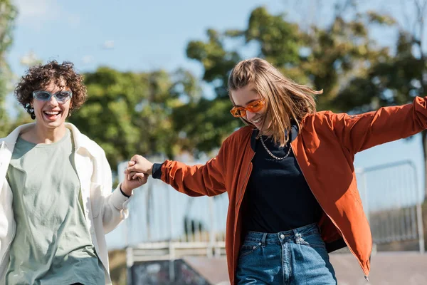 Glückliches junges Paar mit trendiger Sonnenbrille, Händchen haltend im Freien — Stockfoto