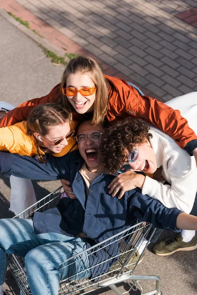 Alto ángulo vista de asiático hombre gritando en compras carro cerca alegre amigos - foto de stock