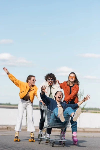 Asian man shouting and gesturing in shopping trolley near excited friends — Stock Photo