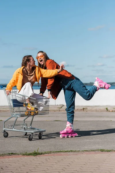 Femme excitée à cheval patins à roulettes près de l'ami dans le panier — Photo de stock