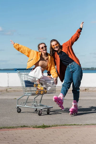 Cheerful rollers with outstretched hands having fun with shopping cart outdoors — Stock Photo
