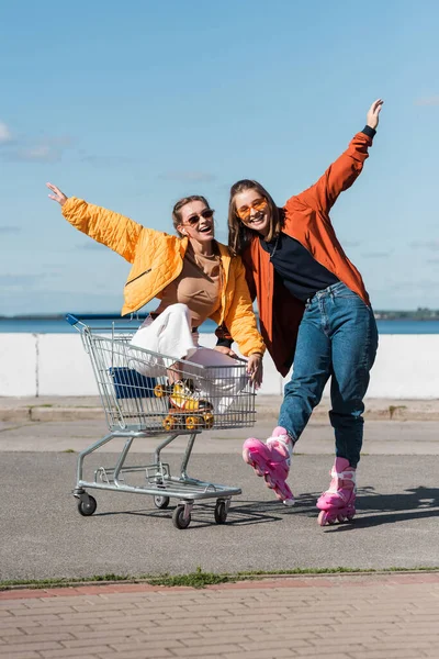 Fröhliche Rollatoren mit ausgestreckten Händen, die Spaß am Einkaufswagen im Freien haben — Stockfoto