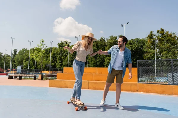 Pareja alegre montando longboard en skate park - foto de stock