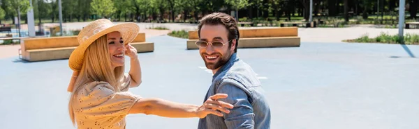 Positive couple in sun hat and sunglasses spending time in skate park, banner — Stock Photo