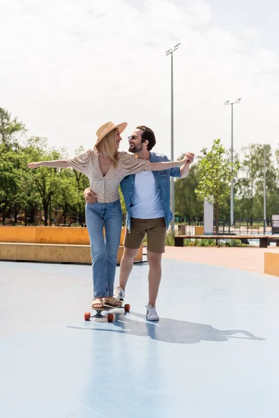 Cheerful couple holding hands and riding longboard in skate park — Stock Photo
