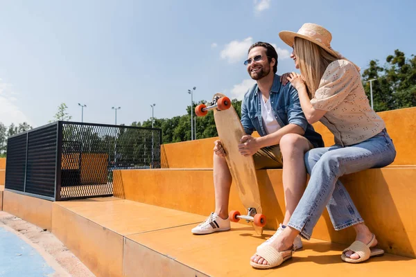 Pareja positiva con longboard sentado en skate park - foto de stock