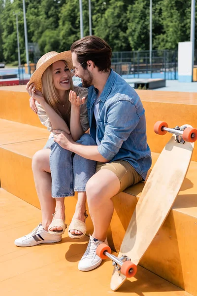 Sorridente coppia parlando e abbracciando vicino longboard in skate park — Foto stock