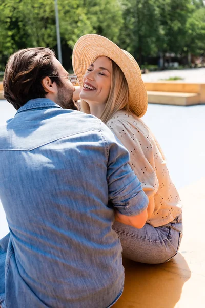 Positive woman in sun hat sitting near boyfriend in skate park — Stock Photo