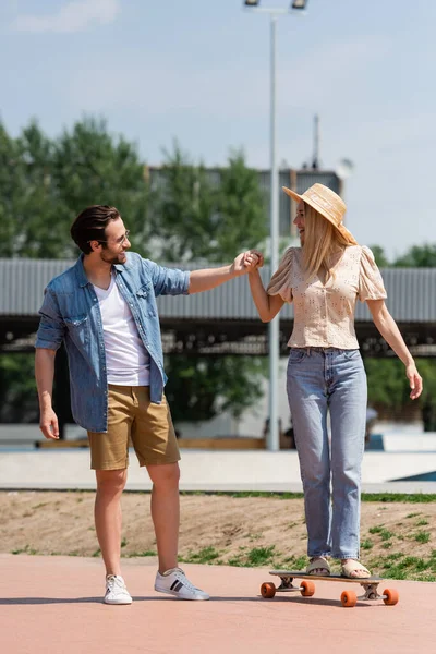 Woman holding hand of boyfriend while riding longboard in skate park — Stock Photo