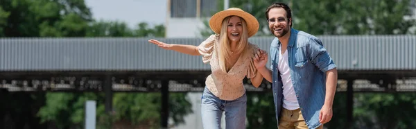 Pareja alegre cogida de la mano y mirando a la cámara al aire libre, pancarta - foto de stock