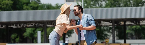Веселая пара в соломенной шляпе и солнцезащитных очках держатся за руки в парке, баннер — стоковое фото