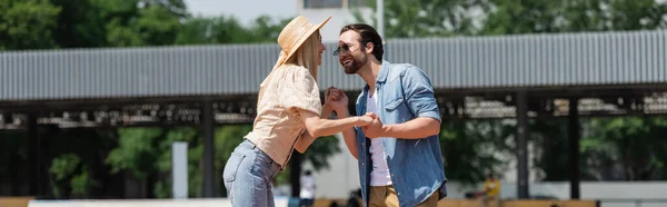 Pareja alegre en sombrero de paja y gafas de sol cogidas de la mano en el parque, pancarta - foto de stock