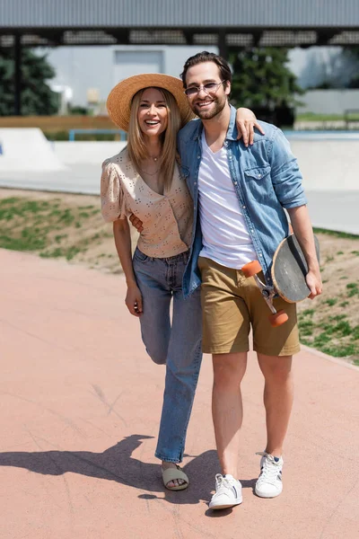 Couple positif étreignant et tenant longboard dans le parc — Photo de stock