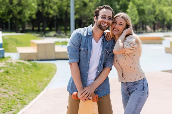 Positives Paar mit Longboard blickt in Skatepark in die Kamera — Stockfoto