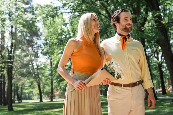 Stilvoller Mann umarmt Freundin mit Blumenstrauß im Park — Stockfoto