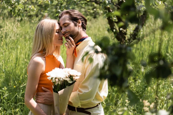 Woman with bouquet touching trendy boyfriend in summer park — Stock Photo