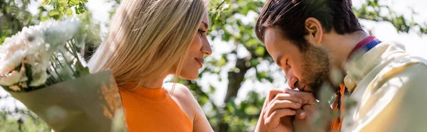 Side view of man kissing hand of girlfriend with bouquet in park, banner — Stock Photo