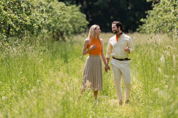 Stylish couple holding hands while talking on meadow in summer park — Stock Photo