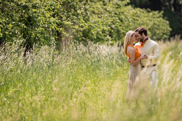 Side view of smiling couple holding hands and hugging on lawn in summer park — Stock Photo