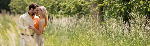 Vue latérale du couple branché se tenant la main et se câlinant dans le parc d'été, bannière — Photo de stock