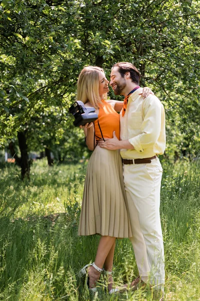 Couple élégant avec caméra rétro étreignant et embrassant dans le parc d'été — Photo de stock