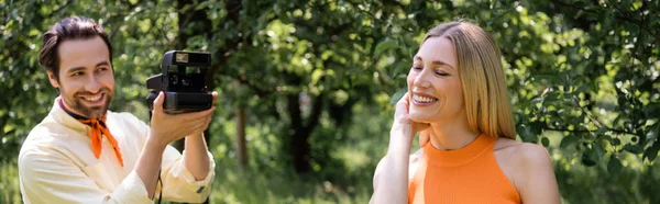 Uomo elegante che scatta foto sulla fotocamera vintage vicino alla ragazza nel parco estivo, banner — Foto stock