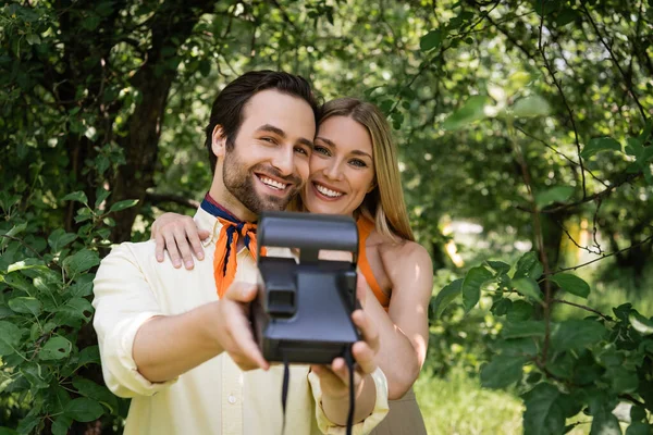 Stylish couple with blurred retro camera smiling in summer park — Stock Photo