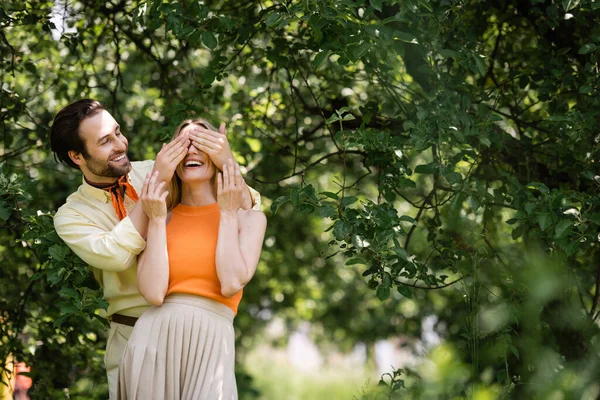 Stylischer Mann verdeckt Augen vor fröhlicher Freundin im Sommerpark — Stockfoto