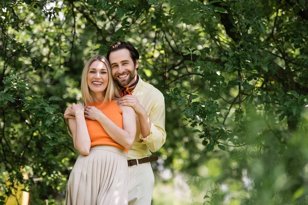 Trendiges romantisches Paar umarmt und lächelt im Sommerpark in die Kamera — Stockfoto