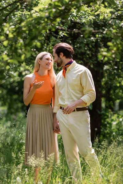 Smiling woman talking to stylish boyfriend while walking in summer park — Stock Photo