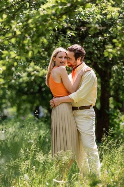 Mujer elegante abrazando novio y mirando a la cámara en el parque de verano - foto de stock