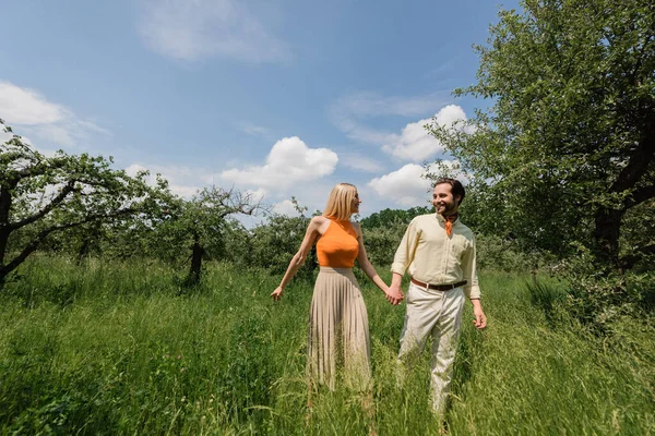 Romantic couple holding hands while walking on meadow in summer park — Stock Photo