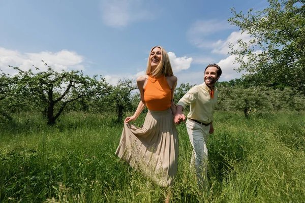 Cheerful woman holding hand of boyfriend on lawn in park — Stock Photo