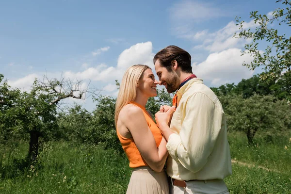 Vue latérale du couple positif et à la mode se tenant la main dans le parc d'été — Photo de stock