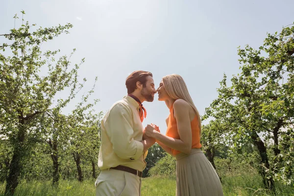 Side view of stylish couple kissing and holding hands in summer park — Stock Photo