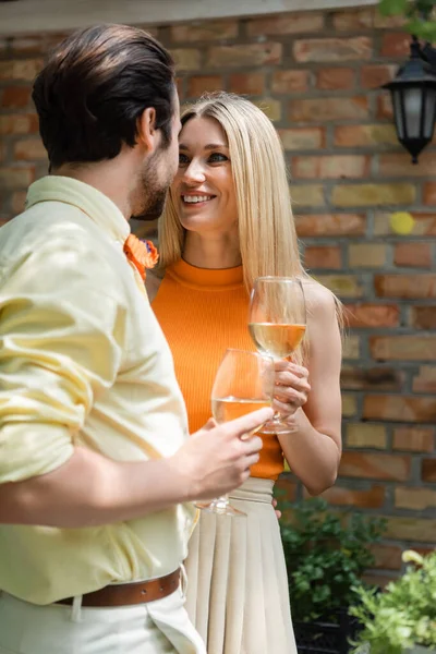 Mujer sonriente sosteniendo copa de vino cerca de novio con estilo en la cafetería al aire libre - foto de stock