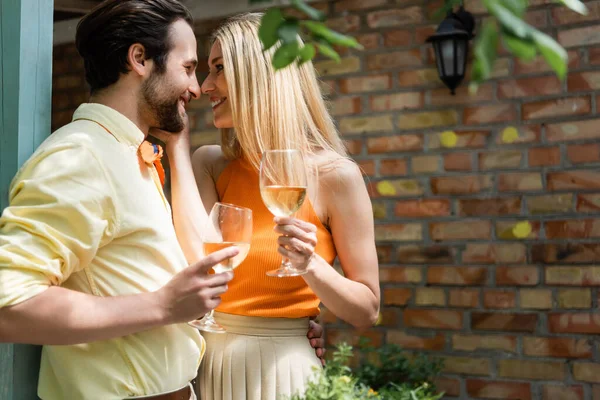 Vista lateral de la sonriente pareja elegante sosteniendo copas de vino en la cafetería al aire libre - foto de stock