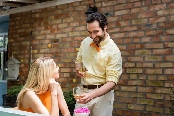 Stylish man holding glasses of wine near smiling girlfriend in outdoor cafe — Stock Photo