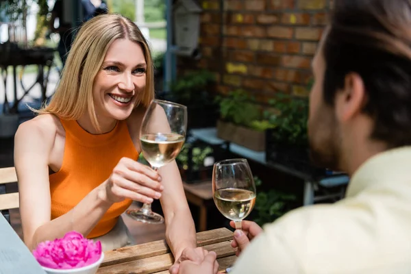 Glückliche Frau hält Glas Wein neben verschwommenem Freund in Outdoor-Café — Stockfoto