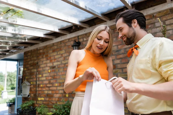 Mujer con estilo mirando bolsa de compras cerca de novio con estilo en la cafetería al aire libre - foto de stock