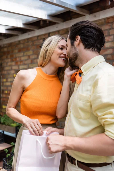 Cheerful woman kissing boyfriend with shopping bag in outdoor cafe — Stock Photo